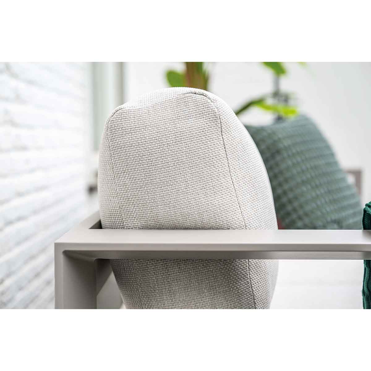 Close-up of a light gray chair with a woven texture and a light gray frame, with another chair in the background.