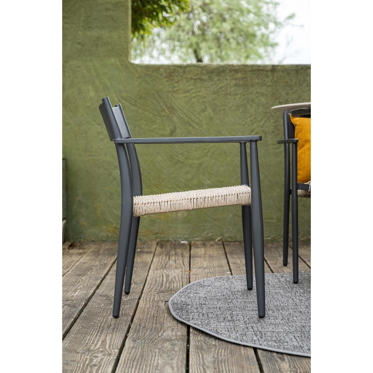 A gray chair with woven seat and back. The chair sits on wooden decking, against a green wall.