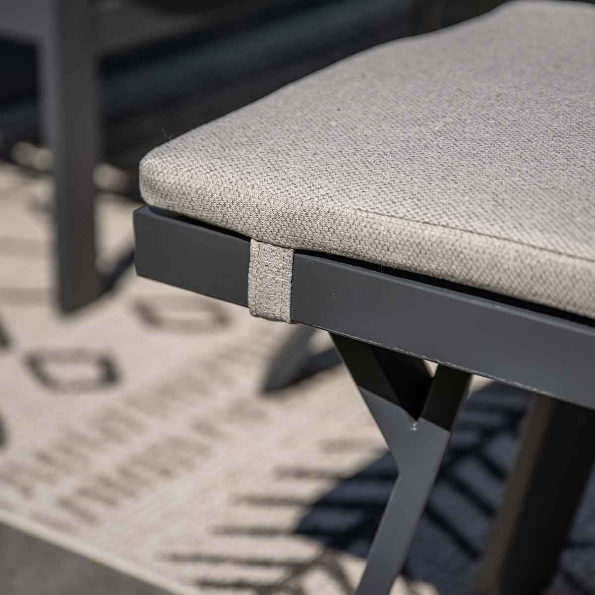 Close-up of a bench with a gray cushion. The frame is gray and the background has a pattern.