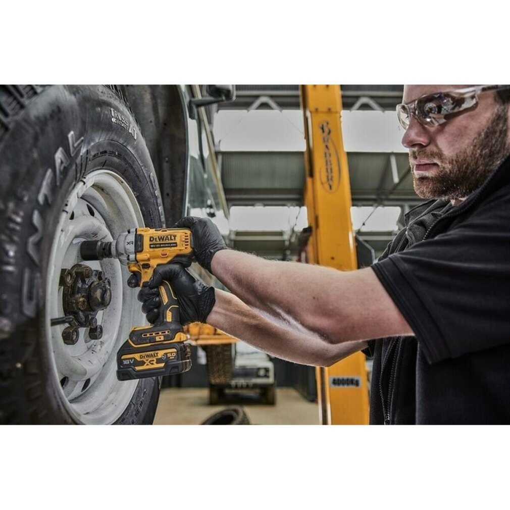 Un hombre usando una llave de impacto DeWalt amarilla y negra en una llanta de coche. Usa guantes y gafas.