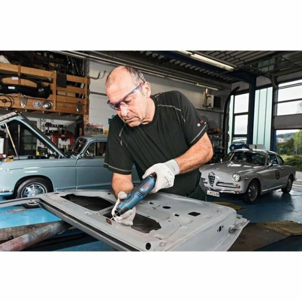Mann, der in einer Garage mit einem Bosch-Rotationswerkzeug an einer Autotür arbeitet.