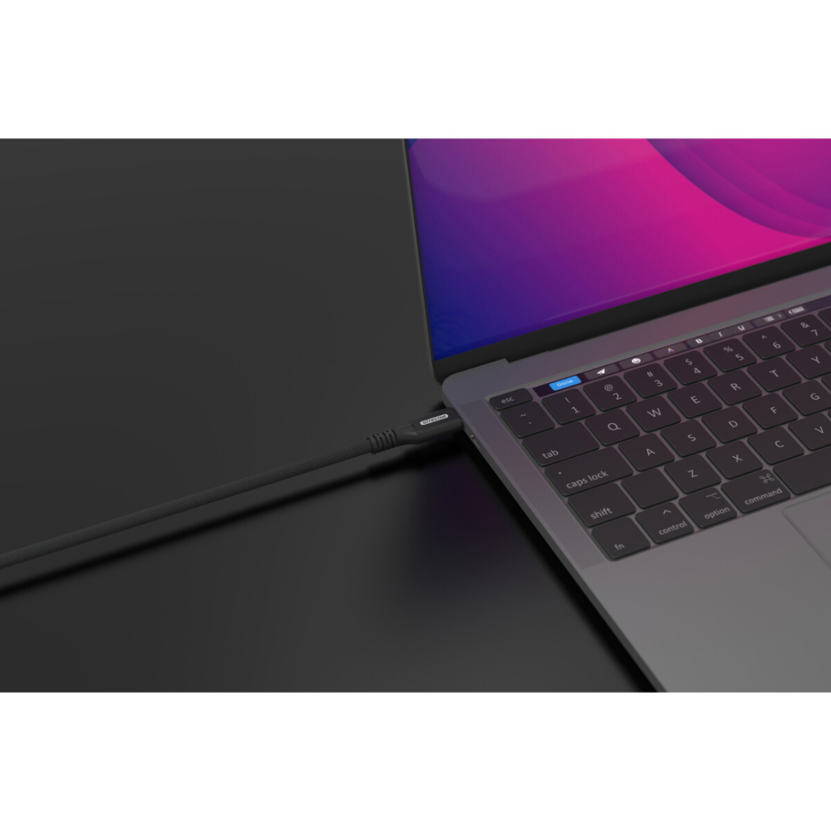 Un laptop collegato a un cavo nero. Il cavo è collegato. Il laptop è su una superficie nera.