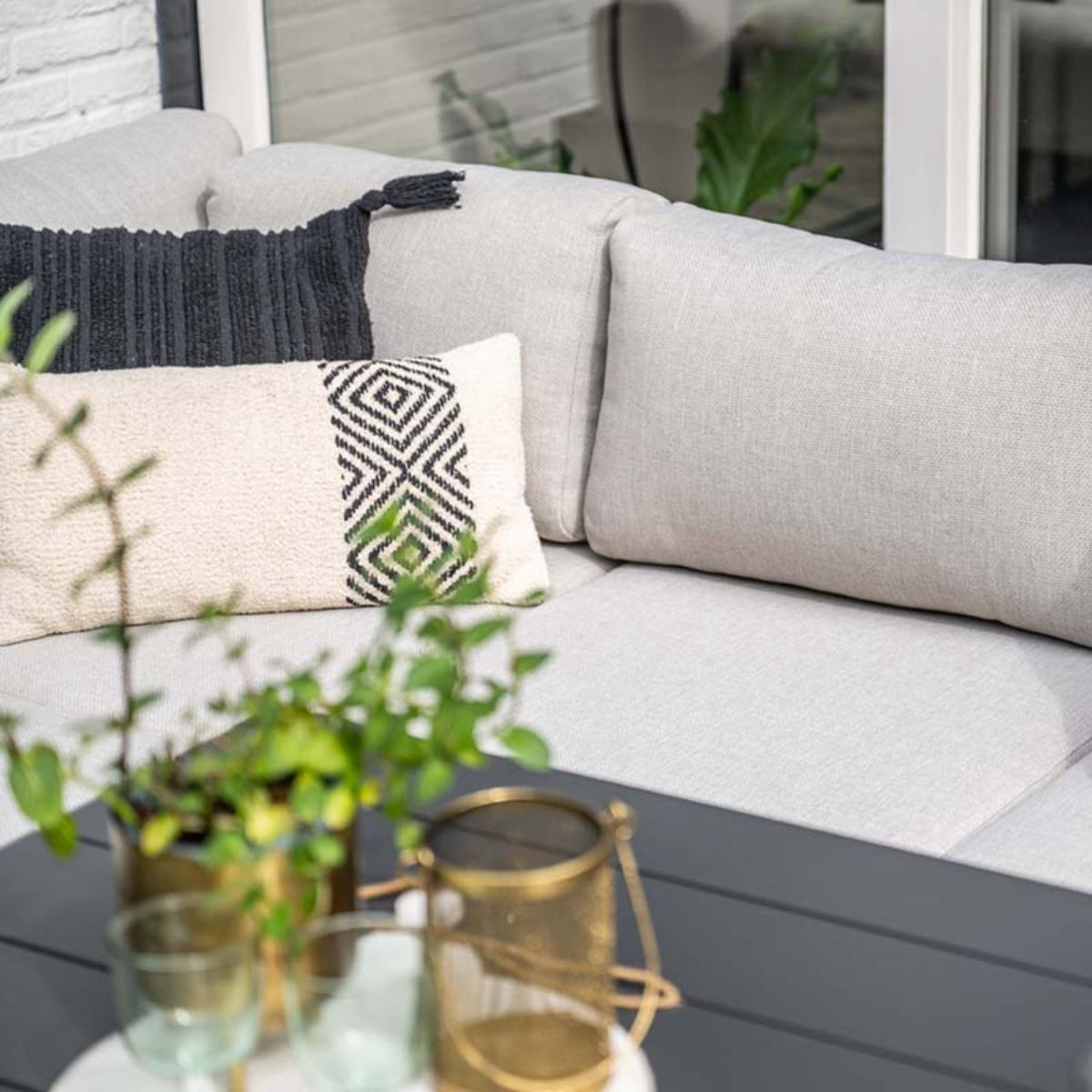 Gros plan d'un canapé extérieur avec coussins, plantes et une table. La scène a une ambiance détendue et accueillante.