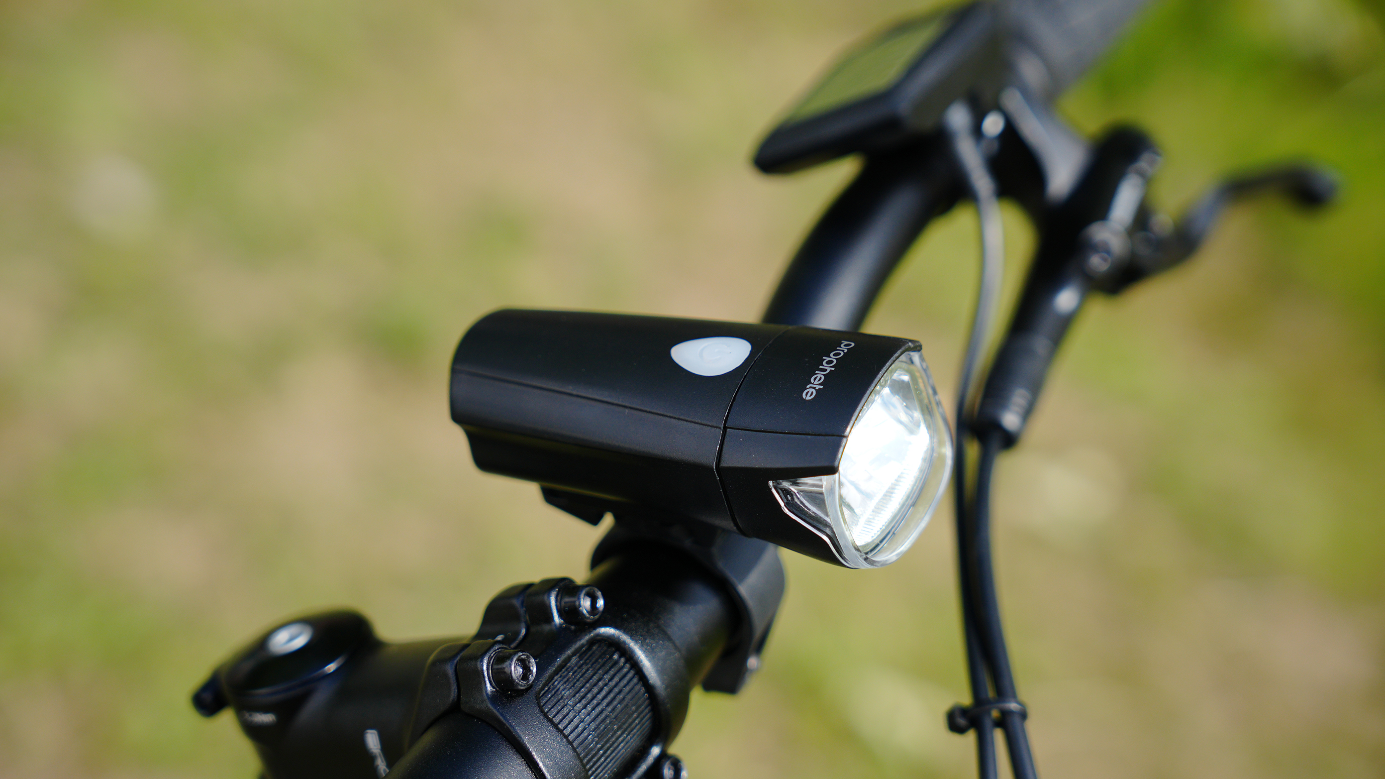 Nahaufnahme eines Fahrradscheinwerfers. Er ist schwarz und am Lenker montiert. Der Hintergrund ist unscharf.