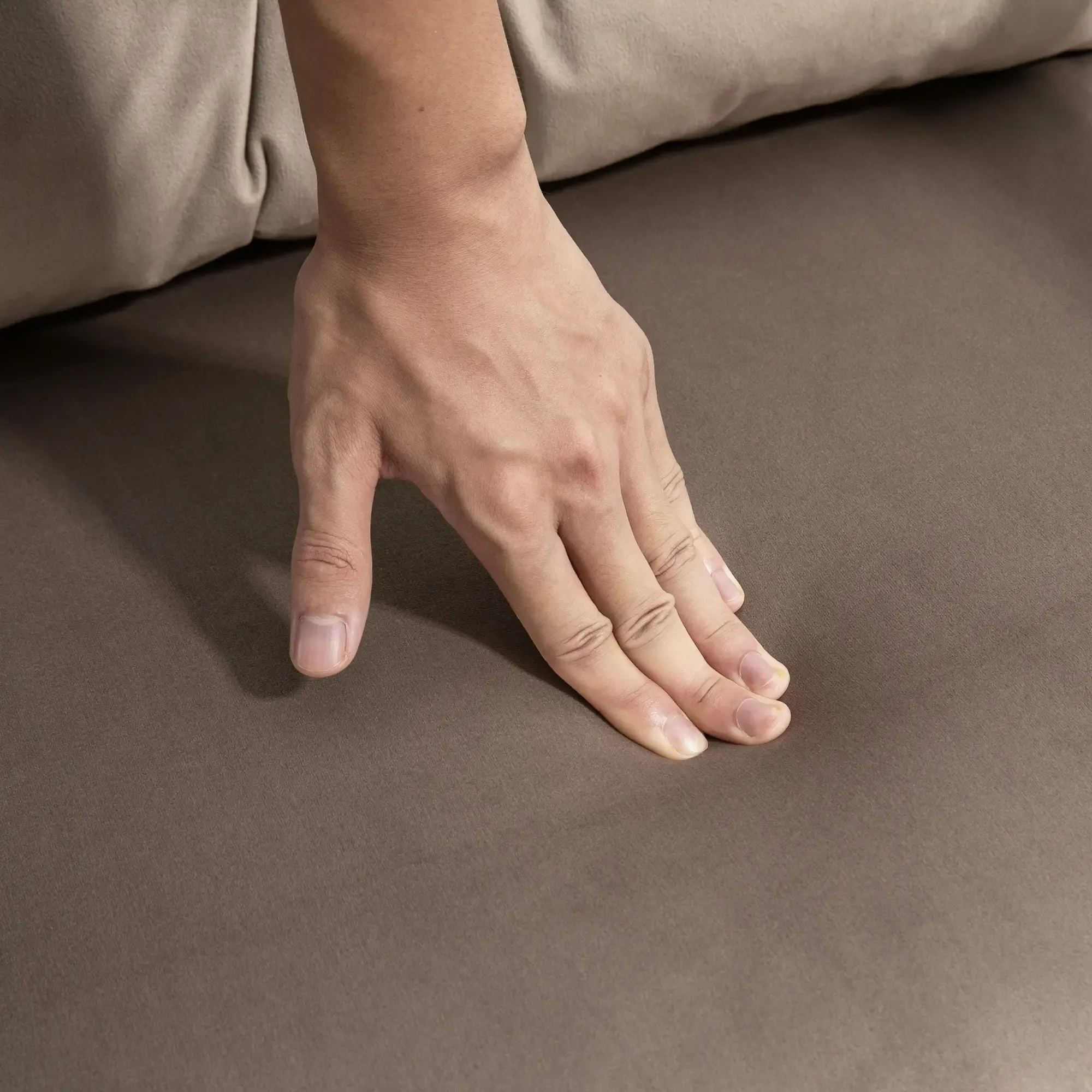 Eine Hand berührt eine braune Oberfläche, möglicherweise Stoff. Die Hand ist offen, die Finger ausgestreckt.