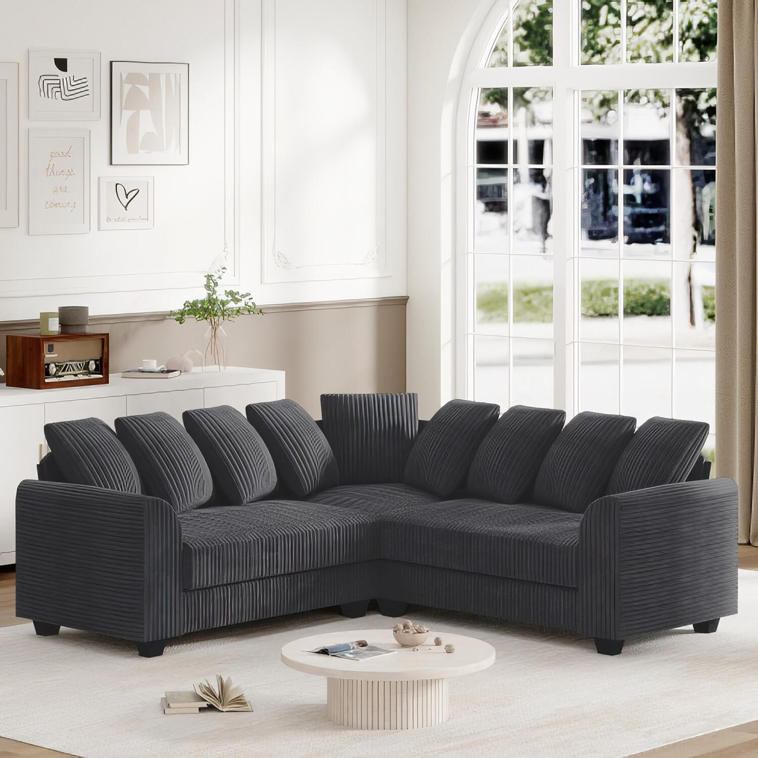 Ein dunkelgraues Ecksofa mit Kissen in einem Raum mit weißem Schrank und Fenster.
