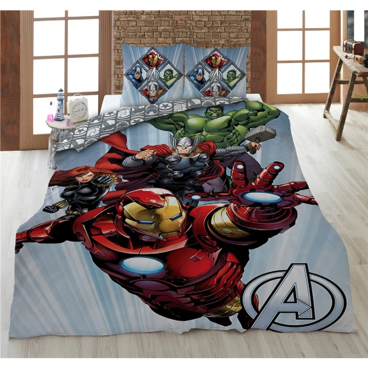 Een bed met een Avengers-thema sprei en twee kussens.