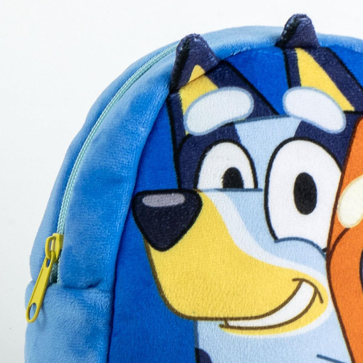 Detalle de la mochila Bluey. Cara de perro de dibujos animados azul y amarillo sonriendo. Cremallera y tela azul claro.