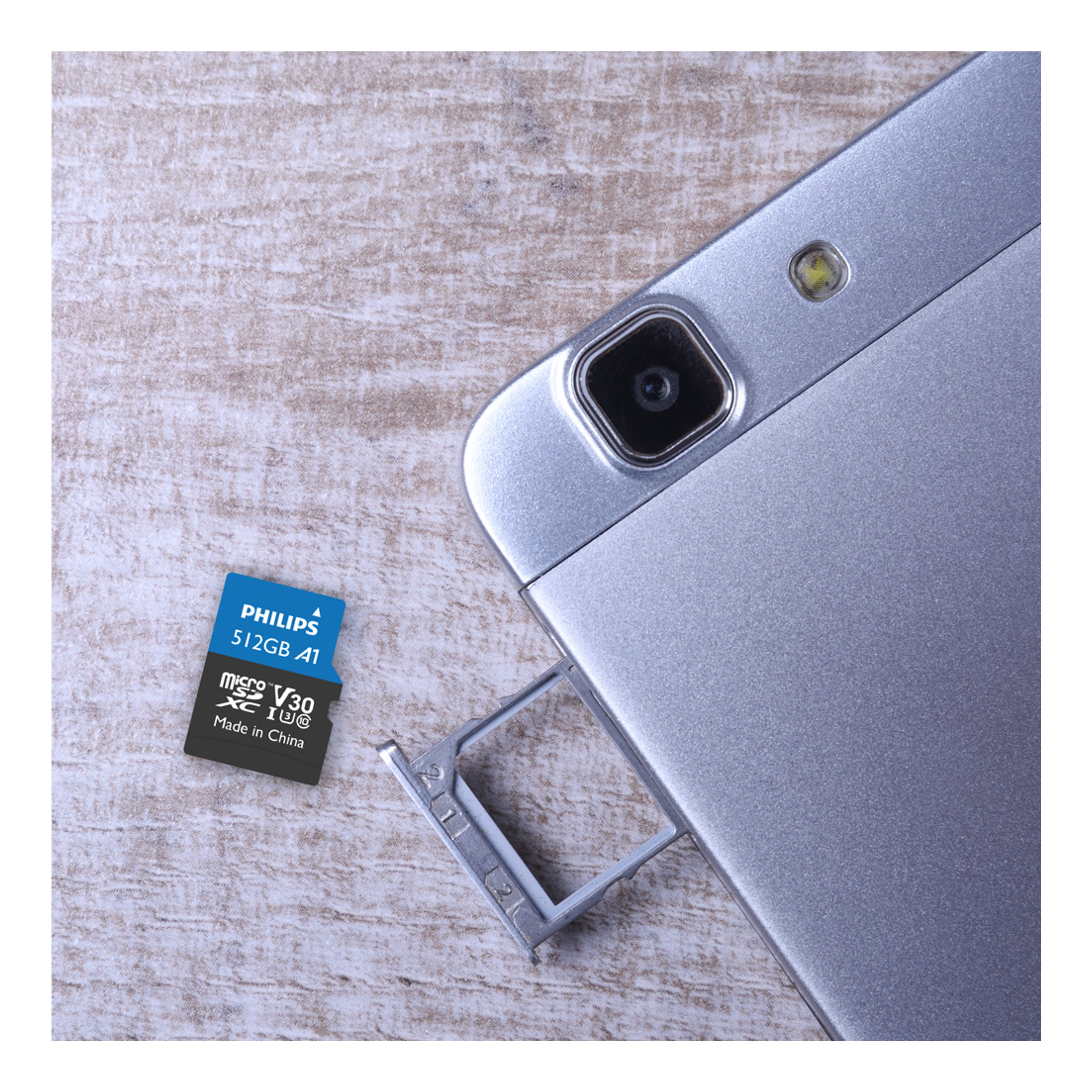 Eine Micro-SD-Karte neben einem silbernen Telefon mit kleiner Kamera. Die SD-Karte hat 512 GB.