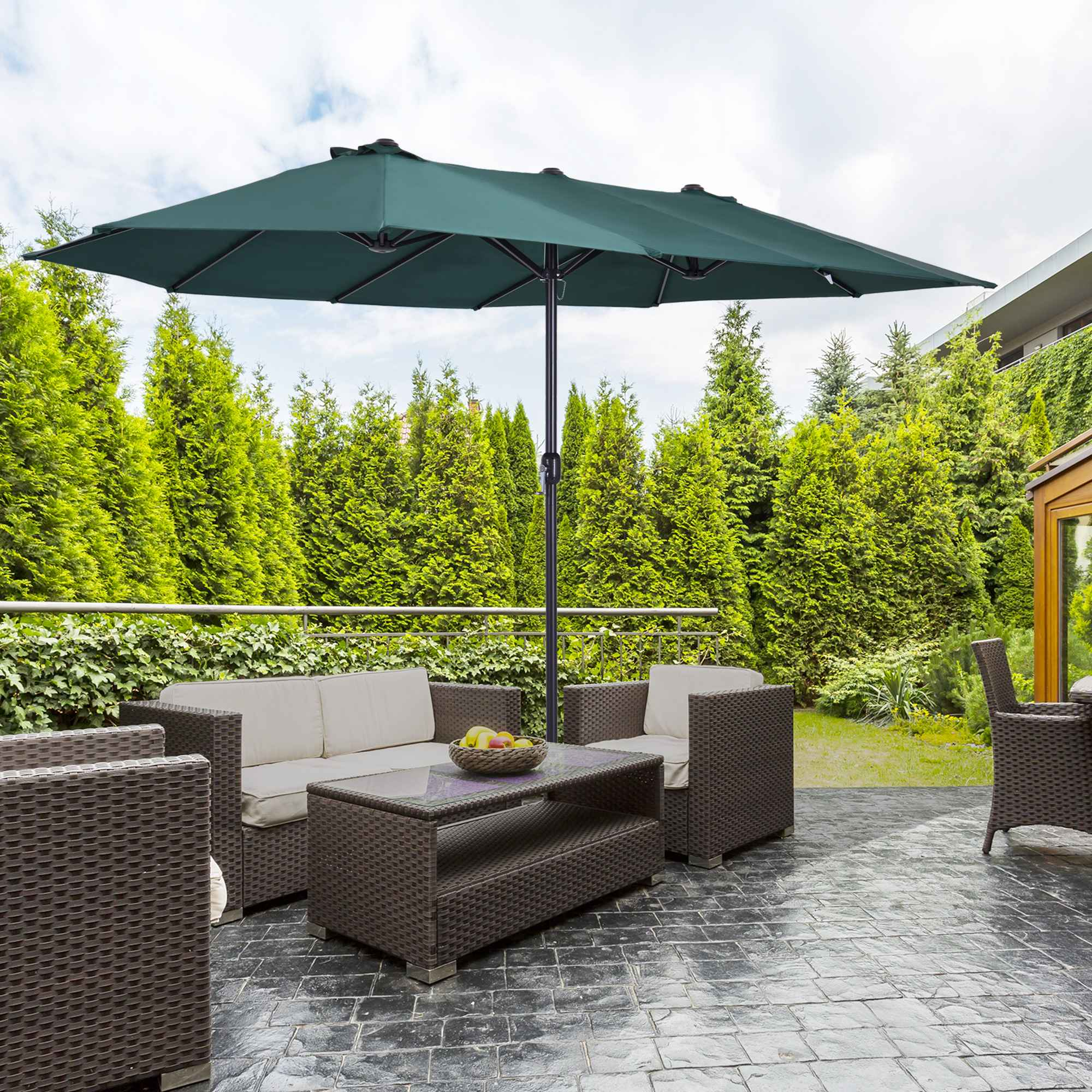 Ein grüner, doppelseitiger Sonnenschirm auf einer Terrasse mit Sitzgelegenheiten und Grün.