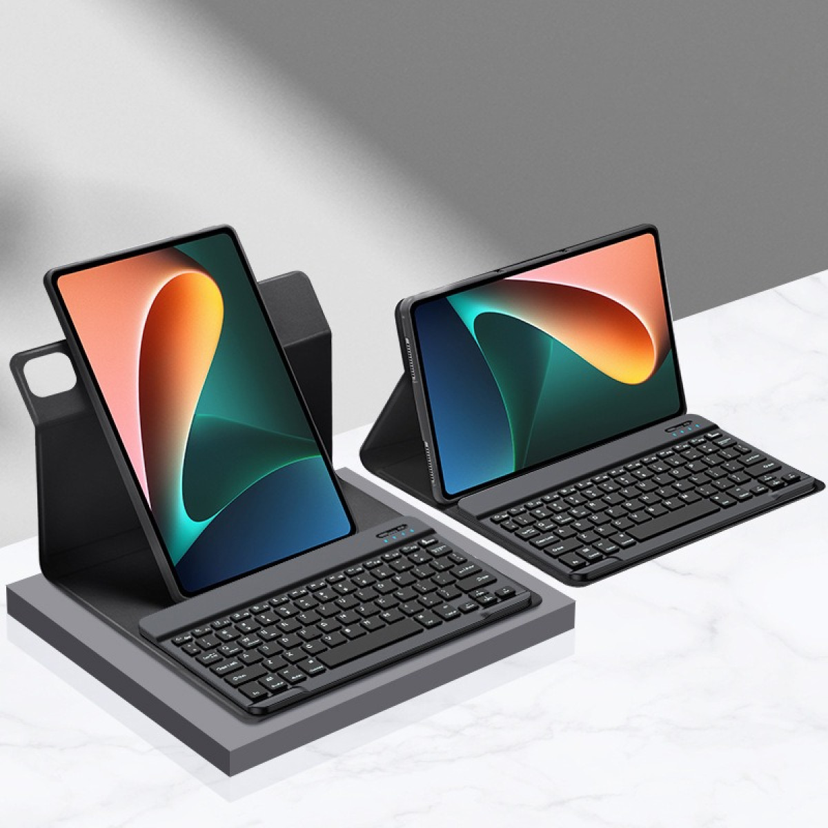 Due tablet con tastiere, angolati su supporti. Gli schermi mostrano immagini colorate.