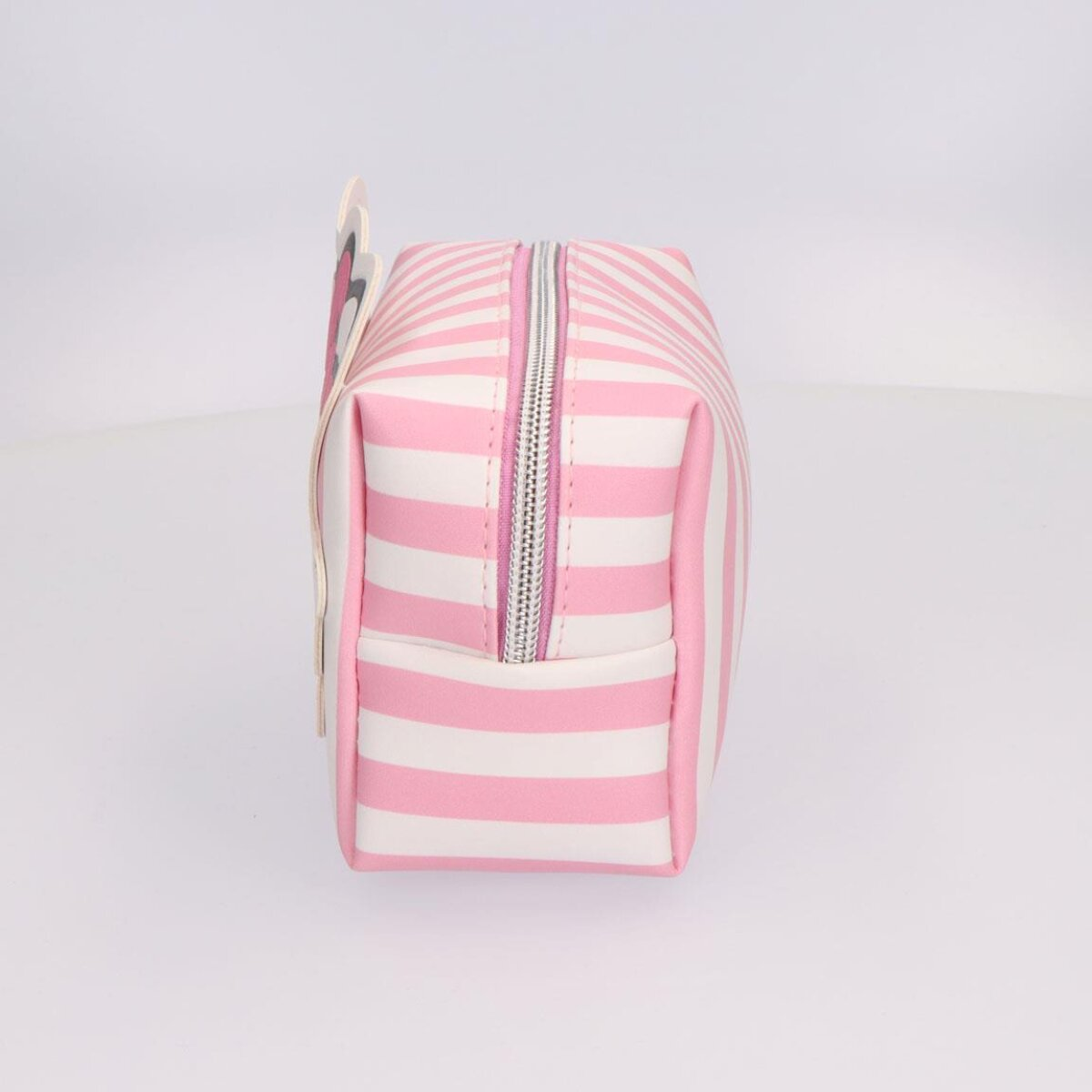 Pink-weiß gestreifte Kosmetiktasche mit Reißverschluss. Ein Anhänger mit Figur ist links.