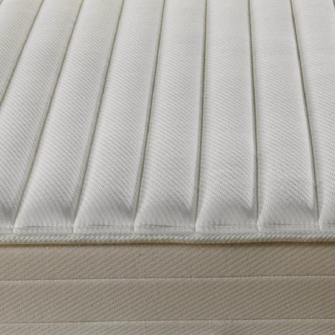 Primer plano de un colchón blanco. La superficie está acolchada con líneas verticales.