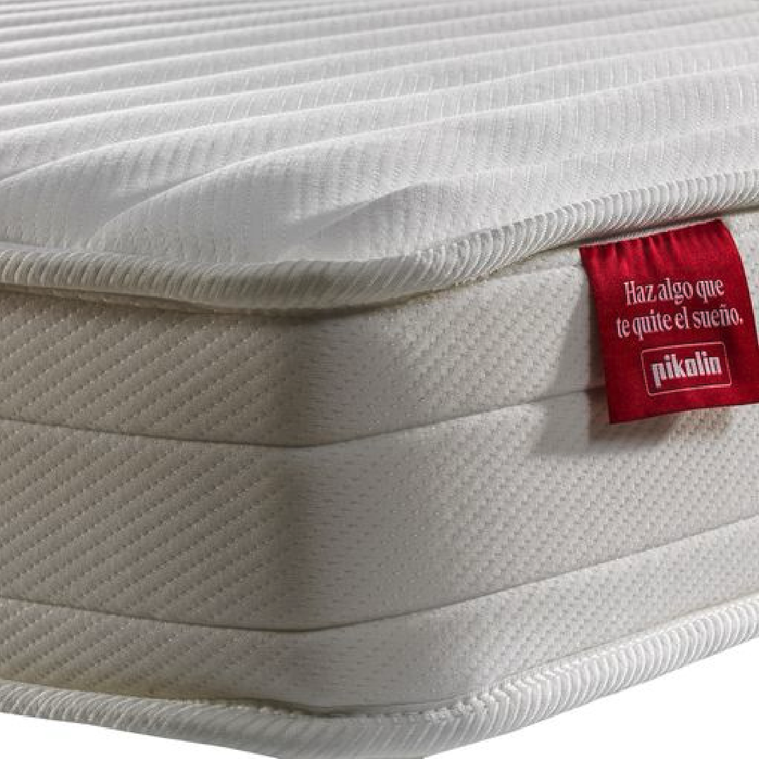 Primer plano de un colchón blanco con superficie acolchada y una etiqueta roja con texto en español.