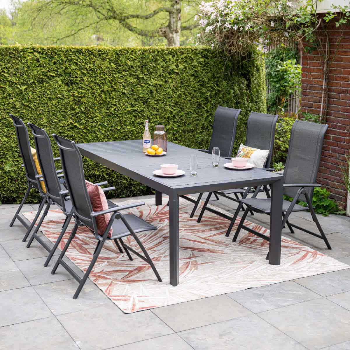 A table set for a meal outdoors with chairs and a green fence.