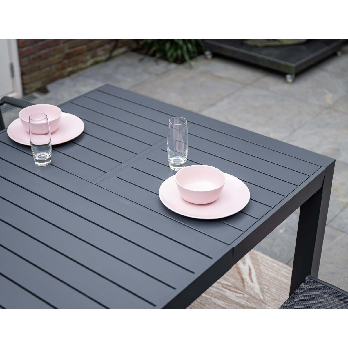 A table set with pink plates, bowls and glasses. Black table with a gray surface.
