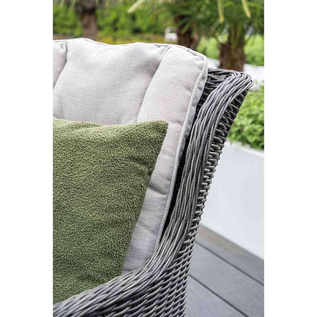 Close-up of wicker chair with gray cushion and green pillow. The chair is on a deck.