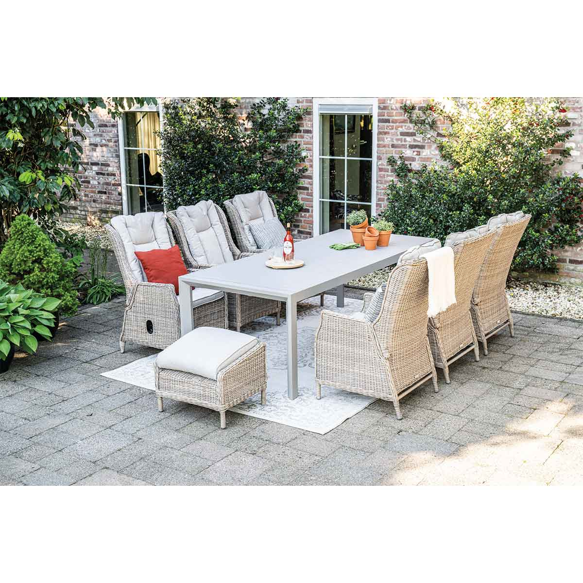 Outdoor dining set with table, chairs, cushions, and a brick background.