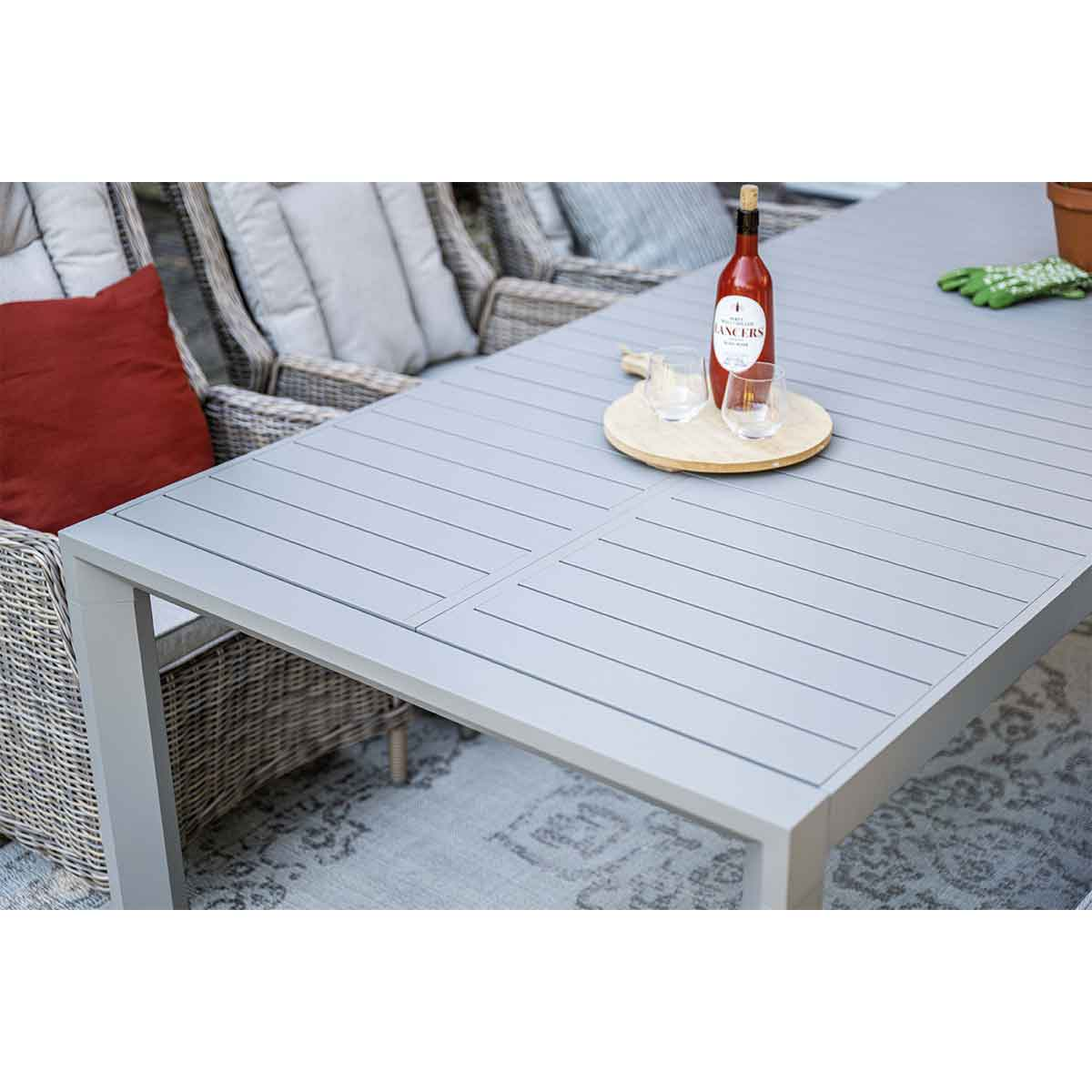 Outdoor table with a bottle of red wine, glasses, and a wooden tray. Gray table and chairs.