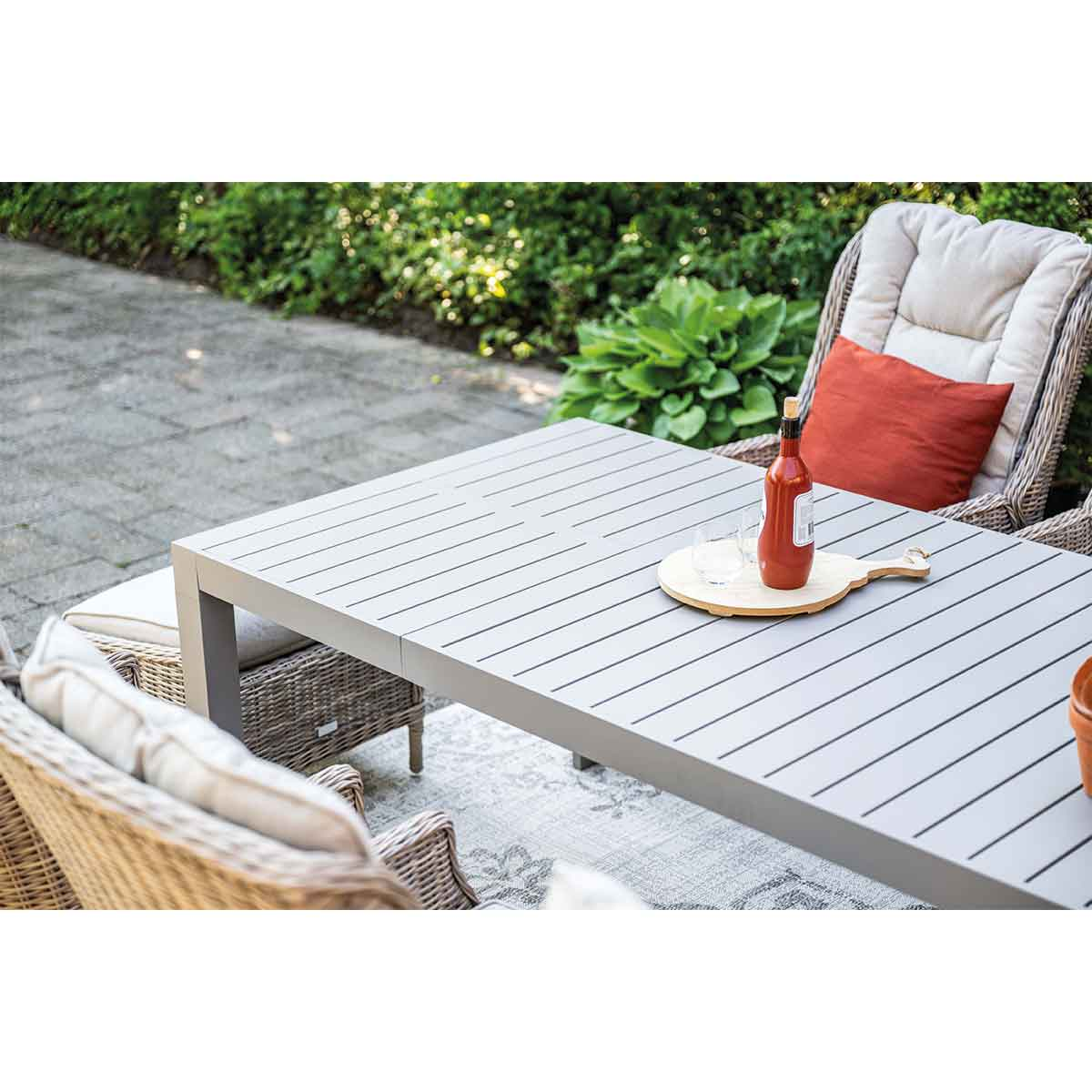 Table setting with wine, glasses, and a tray on a gray table, outdoor setting.