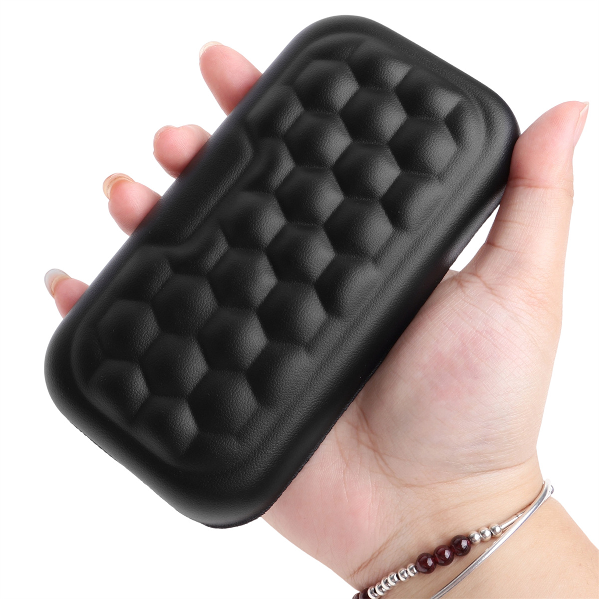 Hand hält eine schwarze Handgelenkstütze. Die Stütze ist schwarz mit Wabenmuster.