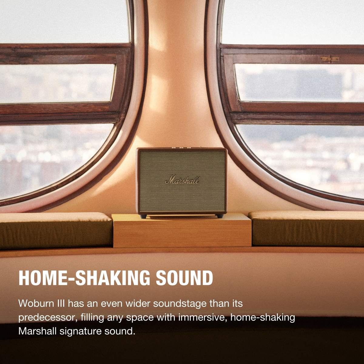 Ein Marshall-Lautsprecher auf einem Holzständer vor einem Fenster. Text: HOME-SHAKING SOUND.