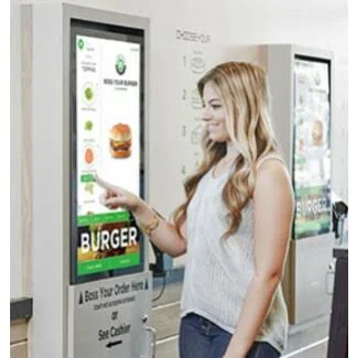 Una donna indica un chiosco di ordinazione touchscreen in un ristorante.