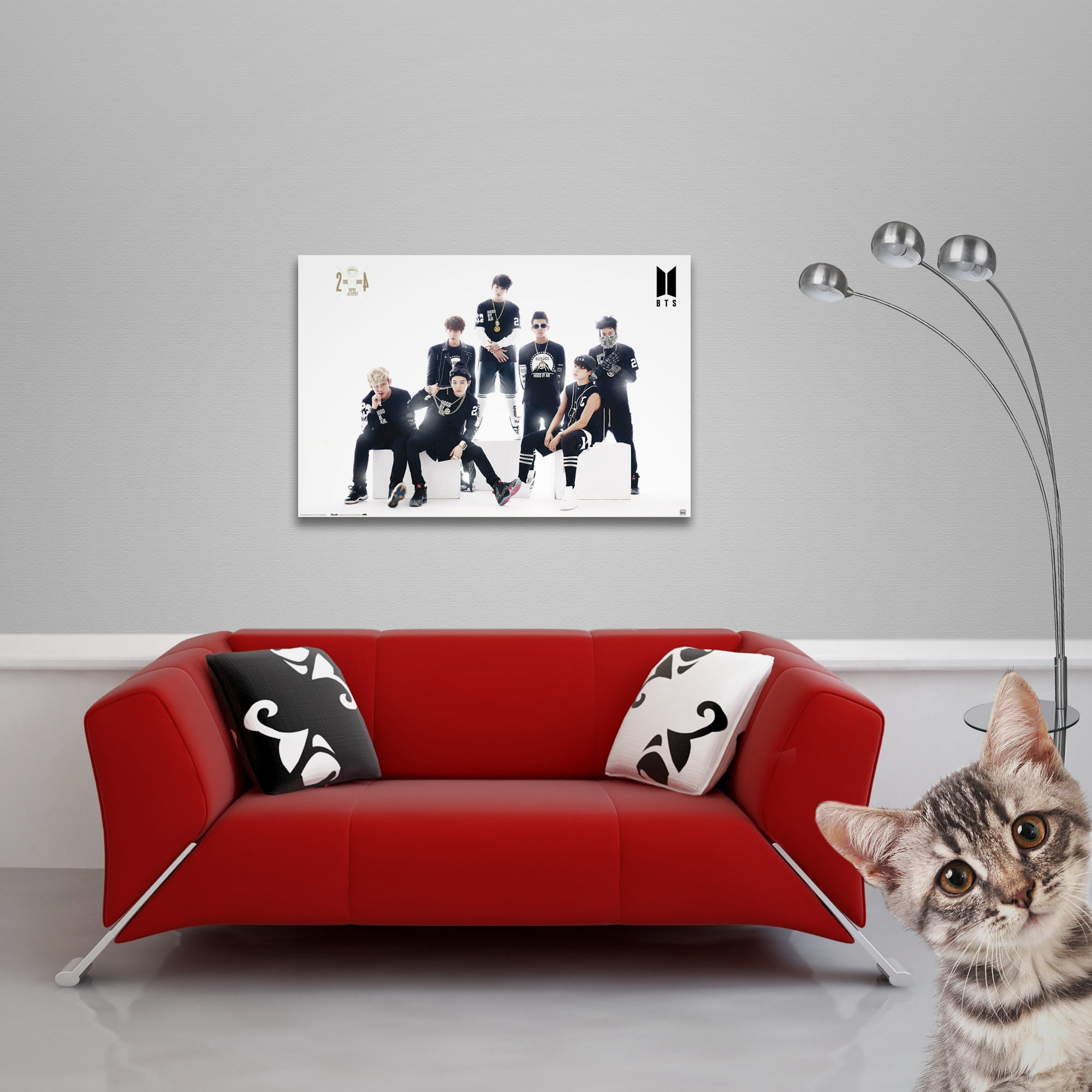 Ein rotes Sofa mit Kissen, ein Bandbild, eine Lampe und eine Katze, die von rechts in einem Raum hervorschaut.