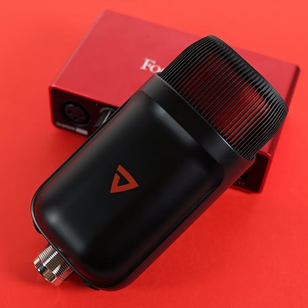 Un microfono nero con logo triangolo rosso su superficie rossa. Una scatola rossa sullo sfondo.