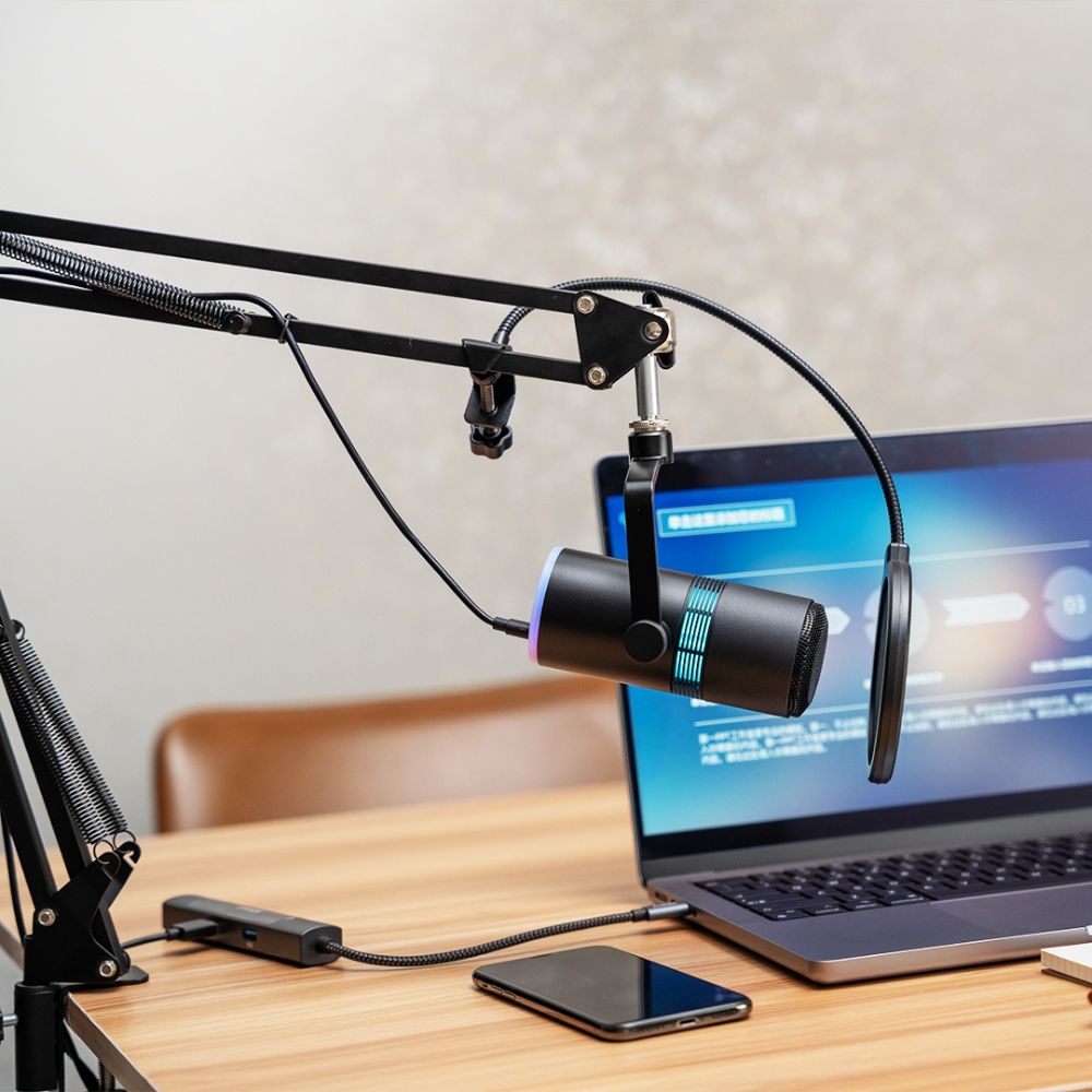 Microfono su un braccio articolato accanto a un laptop. Un telefono e altri oggetti sulla scrivania.