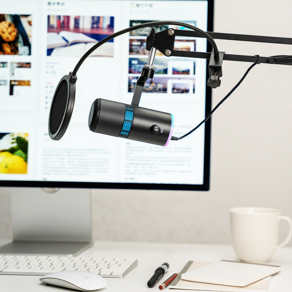 Un microfono su un supporto davanti a un monitor del computer. Mouse, tastiera e tazza di caffè in primo piano.