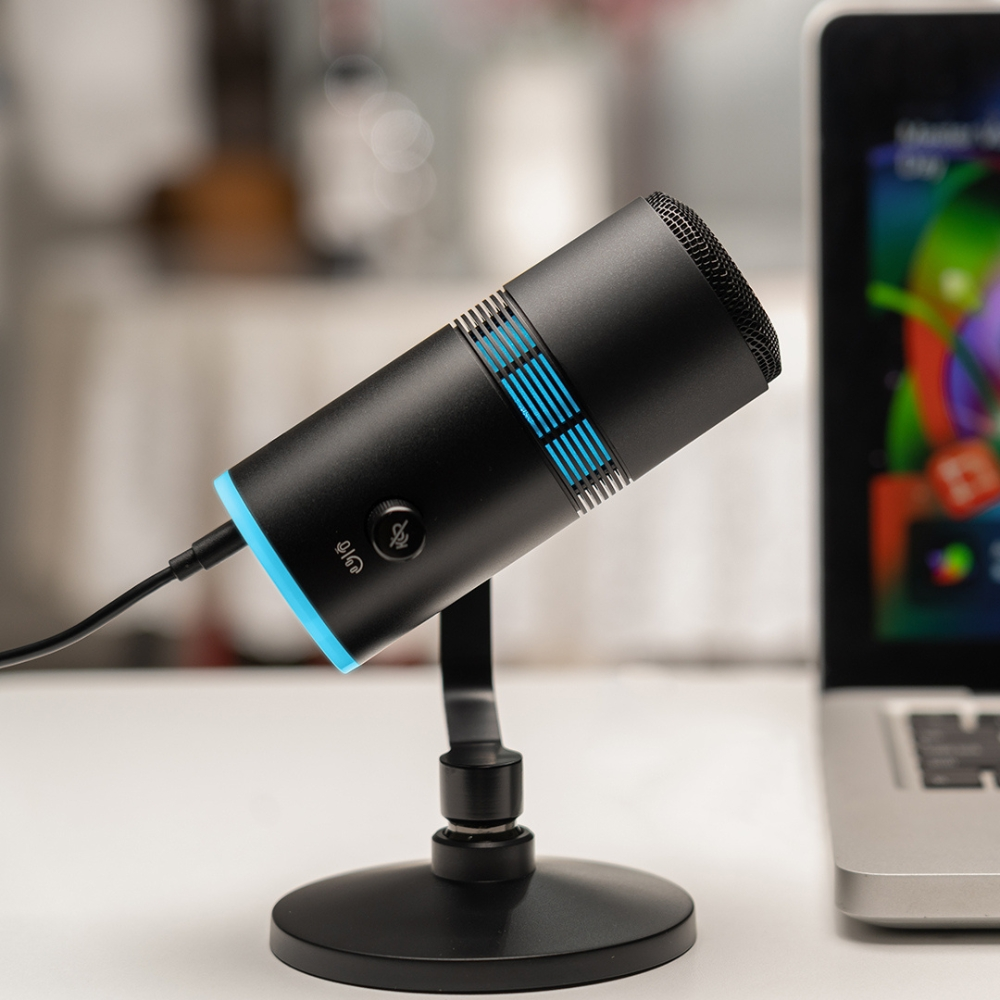 Microfono nero con accenti blu e un laptop. Il microfono è su un supporto.