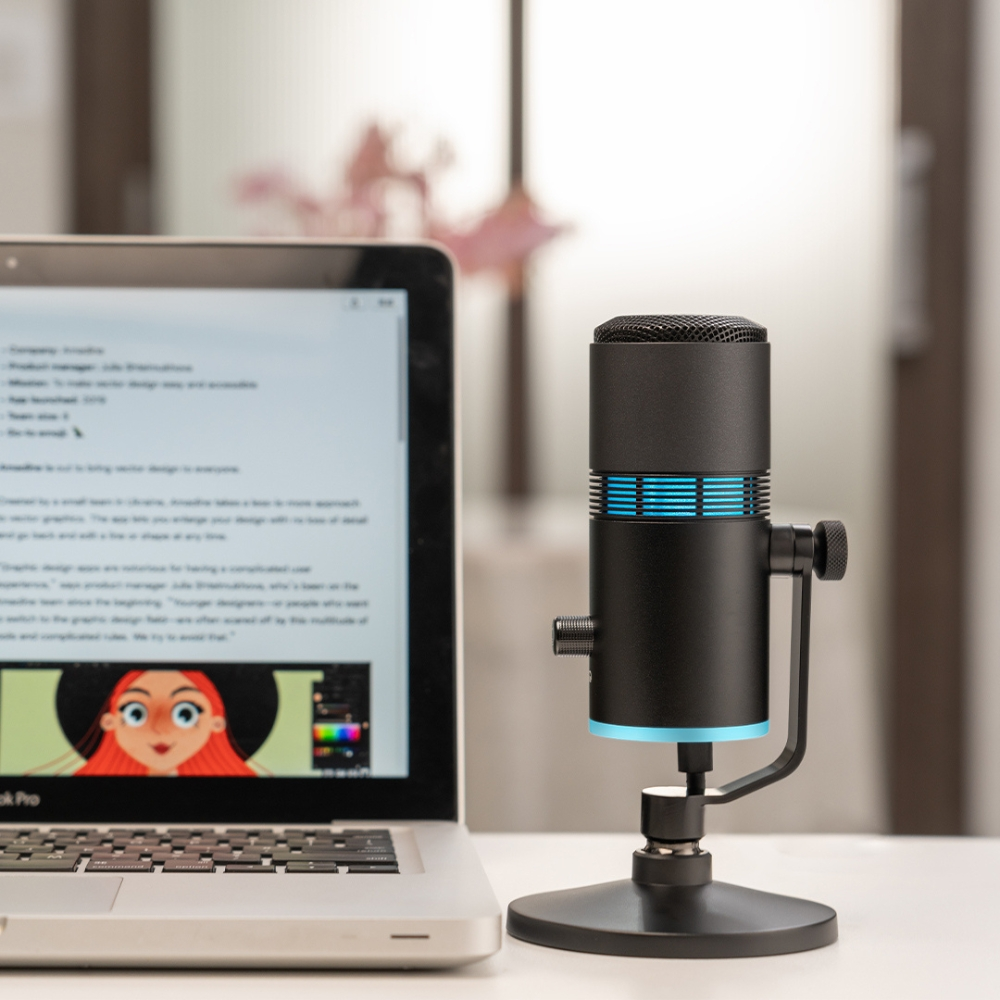 Un microfono nero su un supporto accanto a un laptop. Lo schermo del laptop mostra del testo.