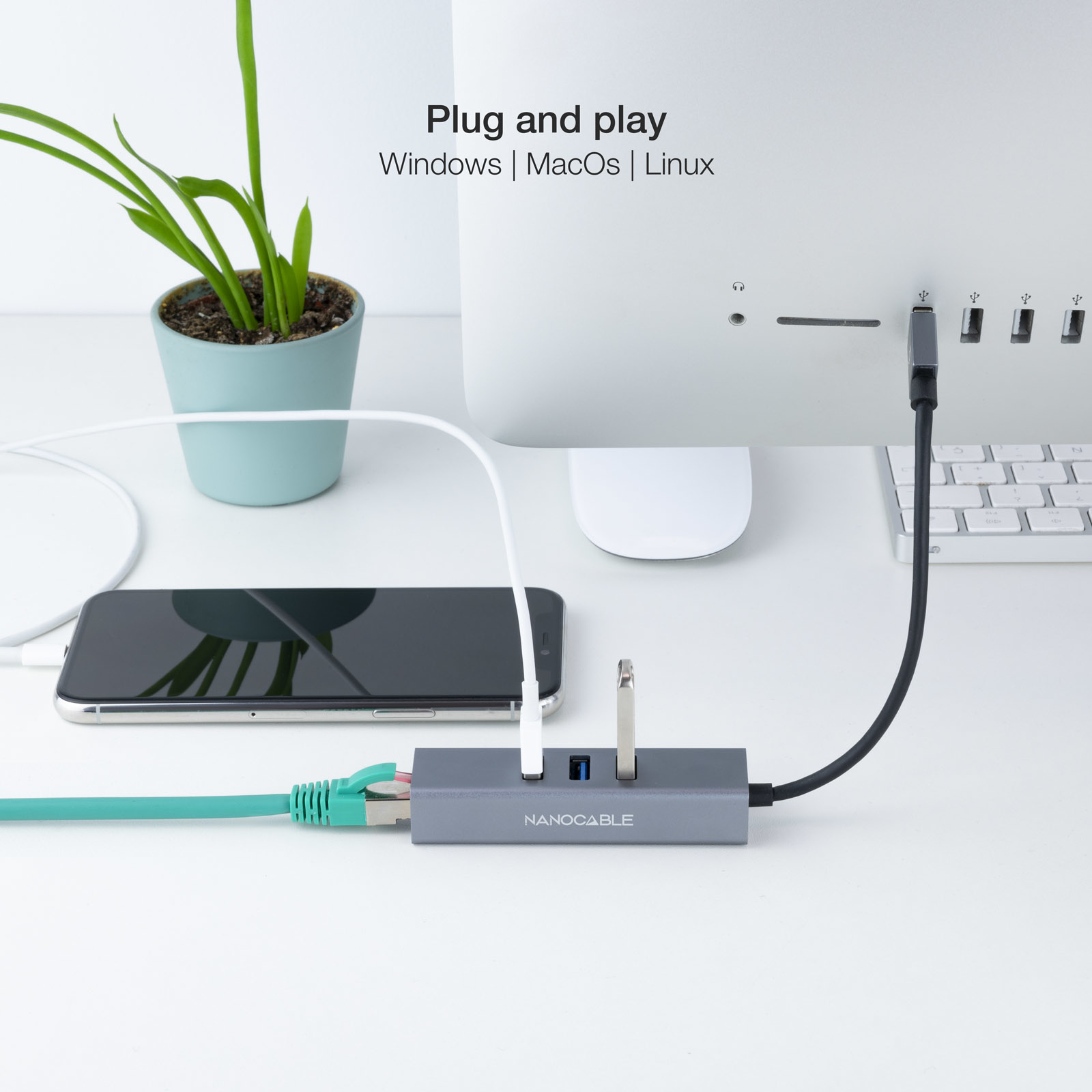 Una configuración de computadora con un monitor, un teléfono y un hub. Todos están conectados a un escritorio, con una planta a la izquierda.