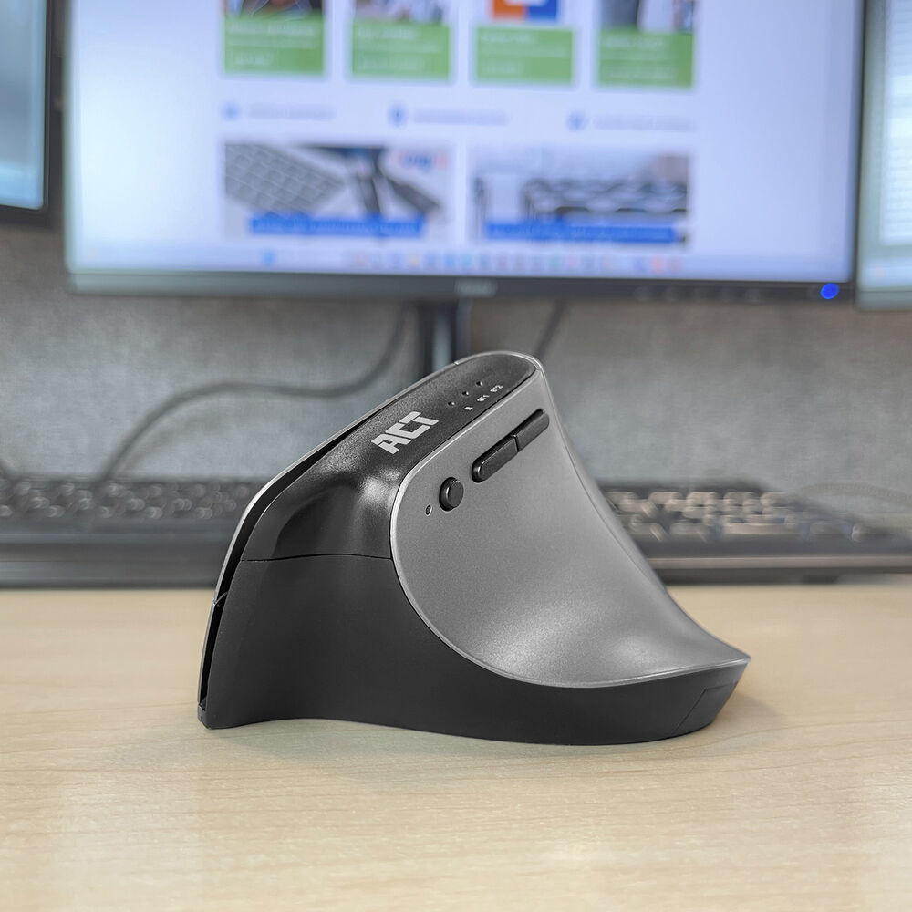 An ergonomic mouse on a wooden desk with a monitor in the background, the mouse is gray and black.