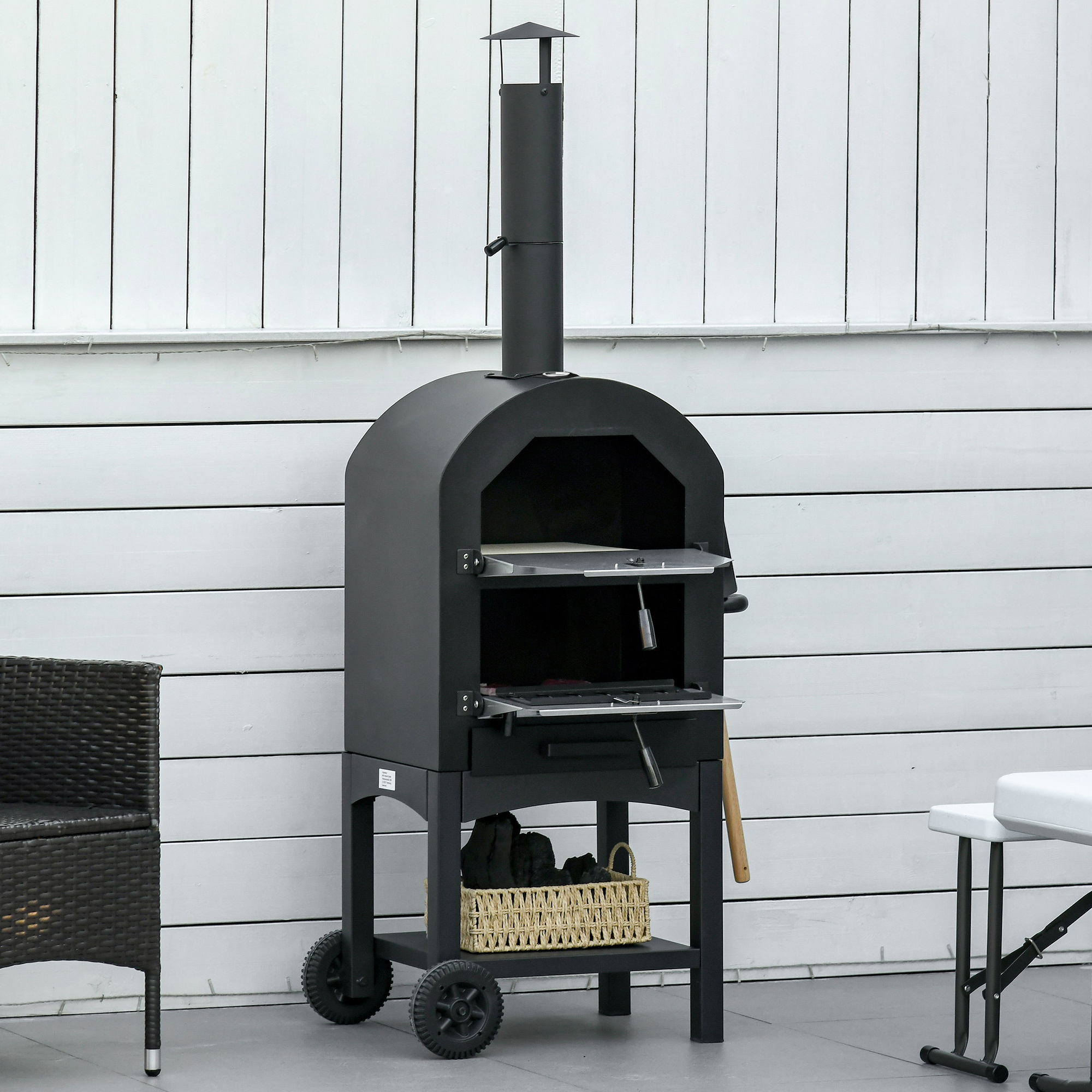 Un forno per pizza nero con un camino si trova su un patio con pareti bianche e mobili in vimini.