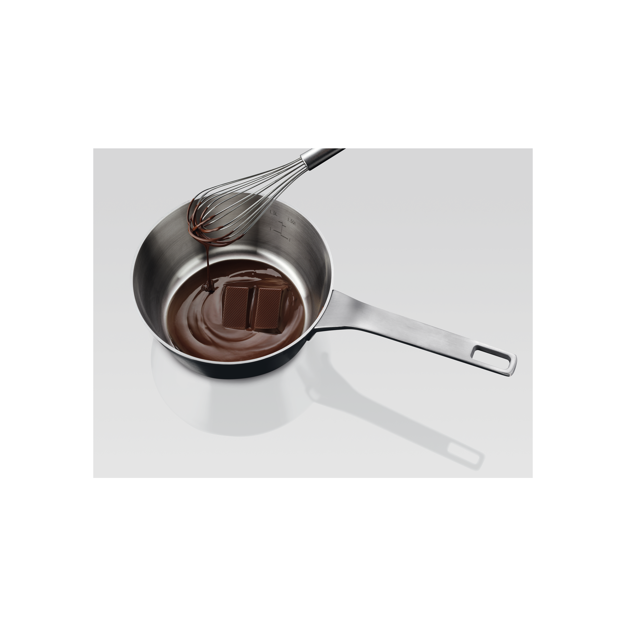 Padella in acciaio inox con cioccolato fuso e pezzi di cioccolato. Frusta. Sfondo bianco con cornice nera.