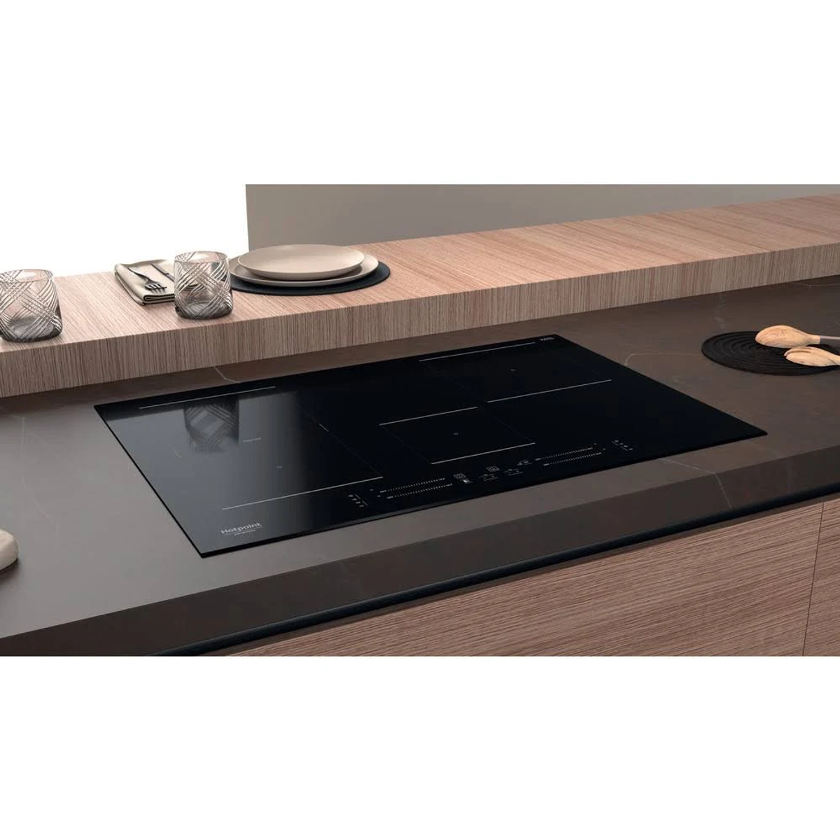 Placa de inducción negra Hotpoint instalada en una encimera de cocina, con vasos y platos.
