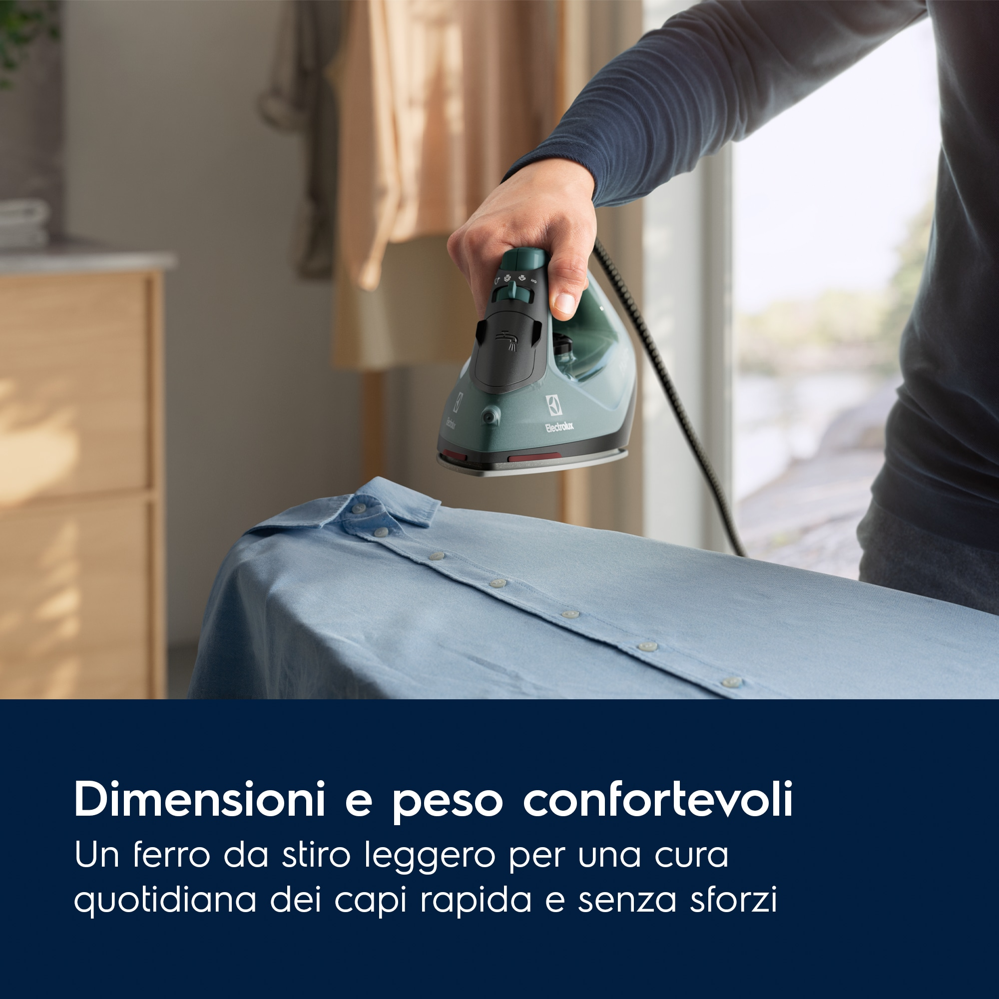 Persona che stira una camicia blu su un'asse da stiro. Finestra sullo sfondo.