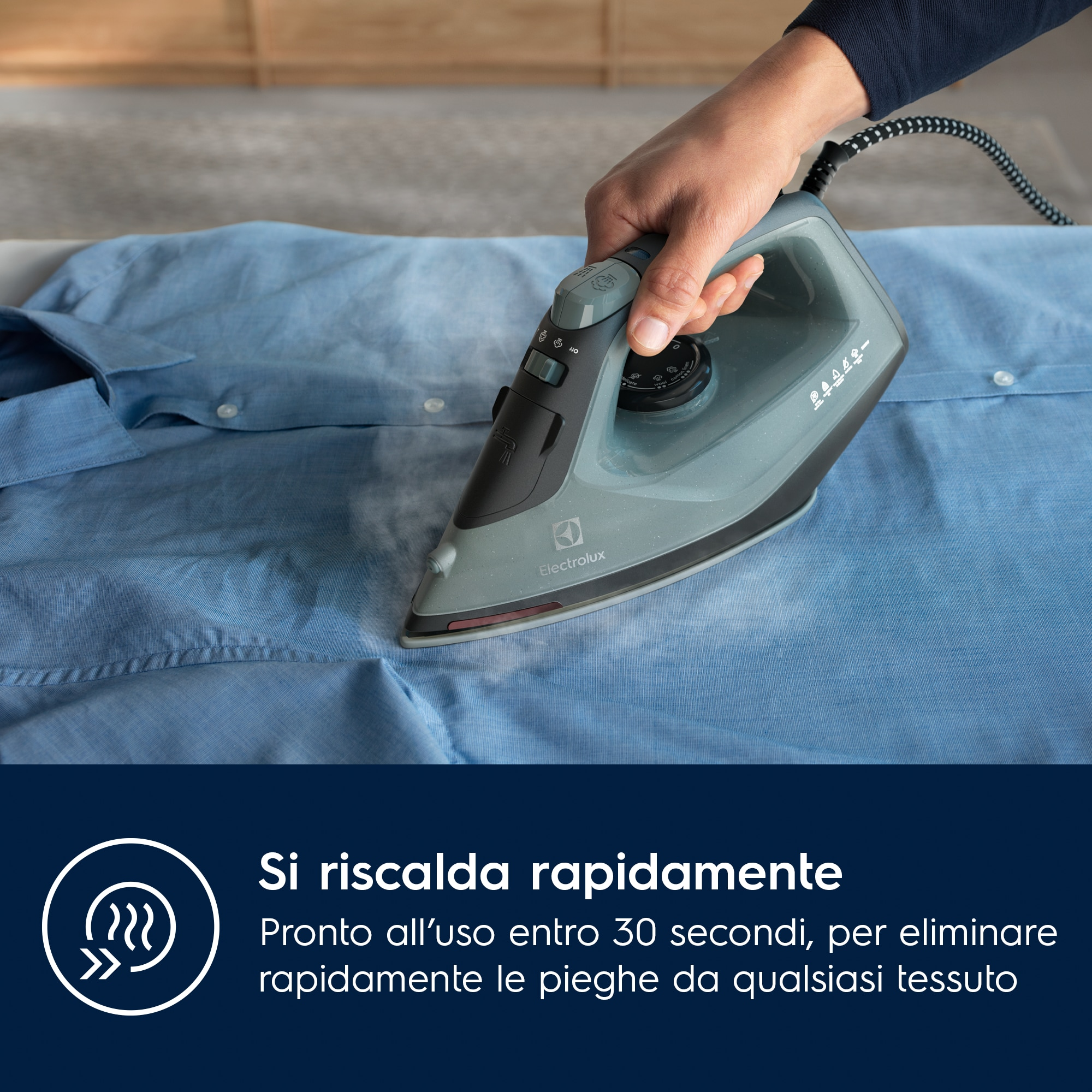 Una persona sta stirando una camicia blu. Il ferro è grigio e nero, il vapore è visibile.