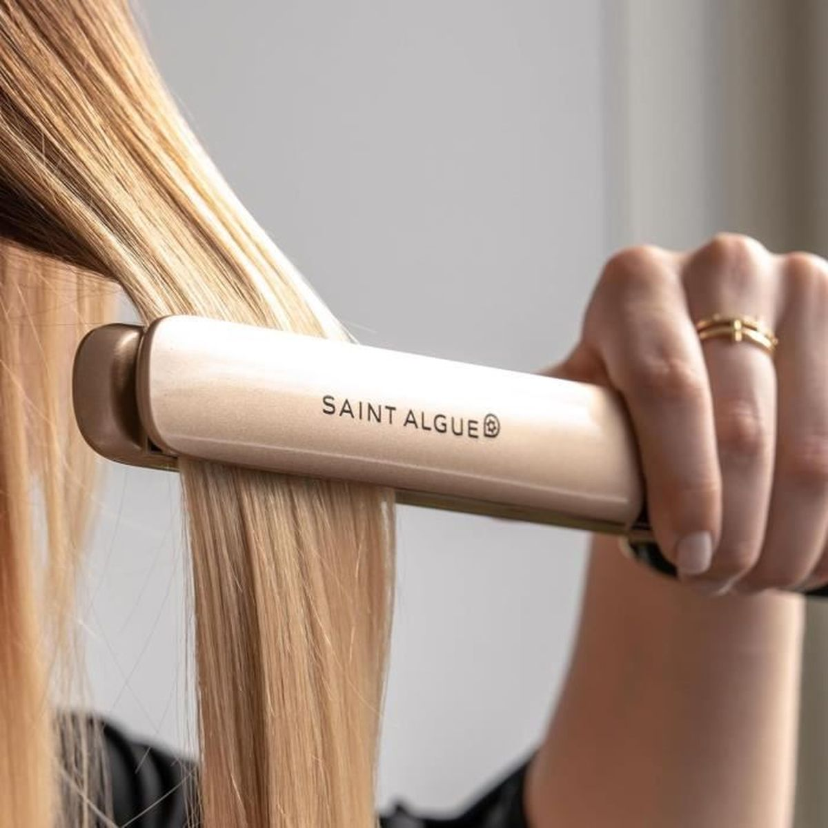 Eine Person benutzt einen goldenen Haarglätter auf einer Strähne blonden Haares.