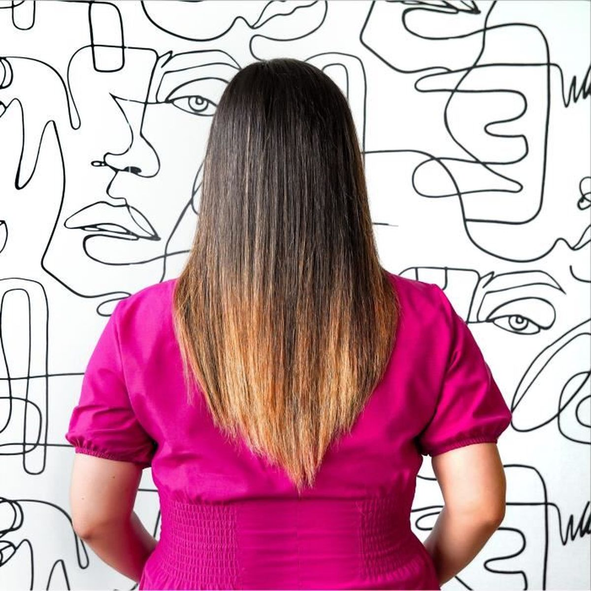 Frau mit langen, glatten Haaren mit blonden Highlights, steht mit dem Rücken zur Kamera.