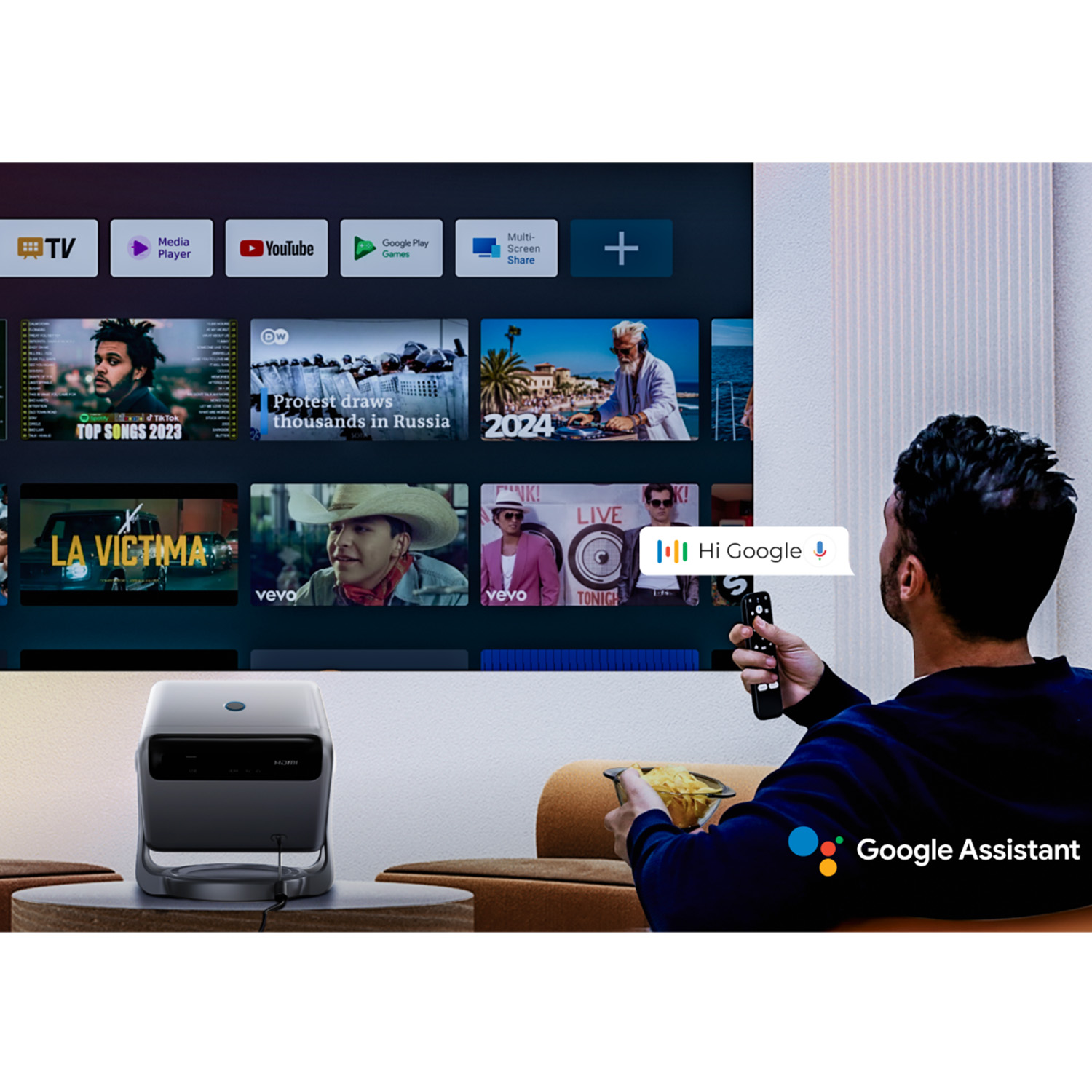 Ein Mann bedient eine Fernbedienung, um mit einem Fernseher zu interagieren. Ein kleiner Projektor steht im Vordergrund. Der Bildschirm zeigt ein Menü.