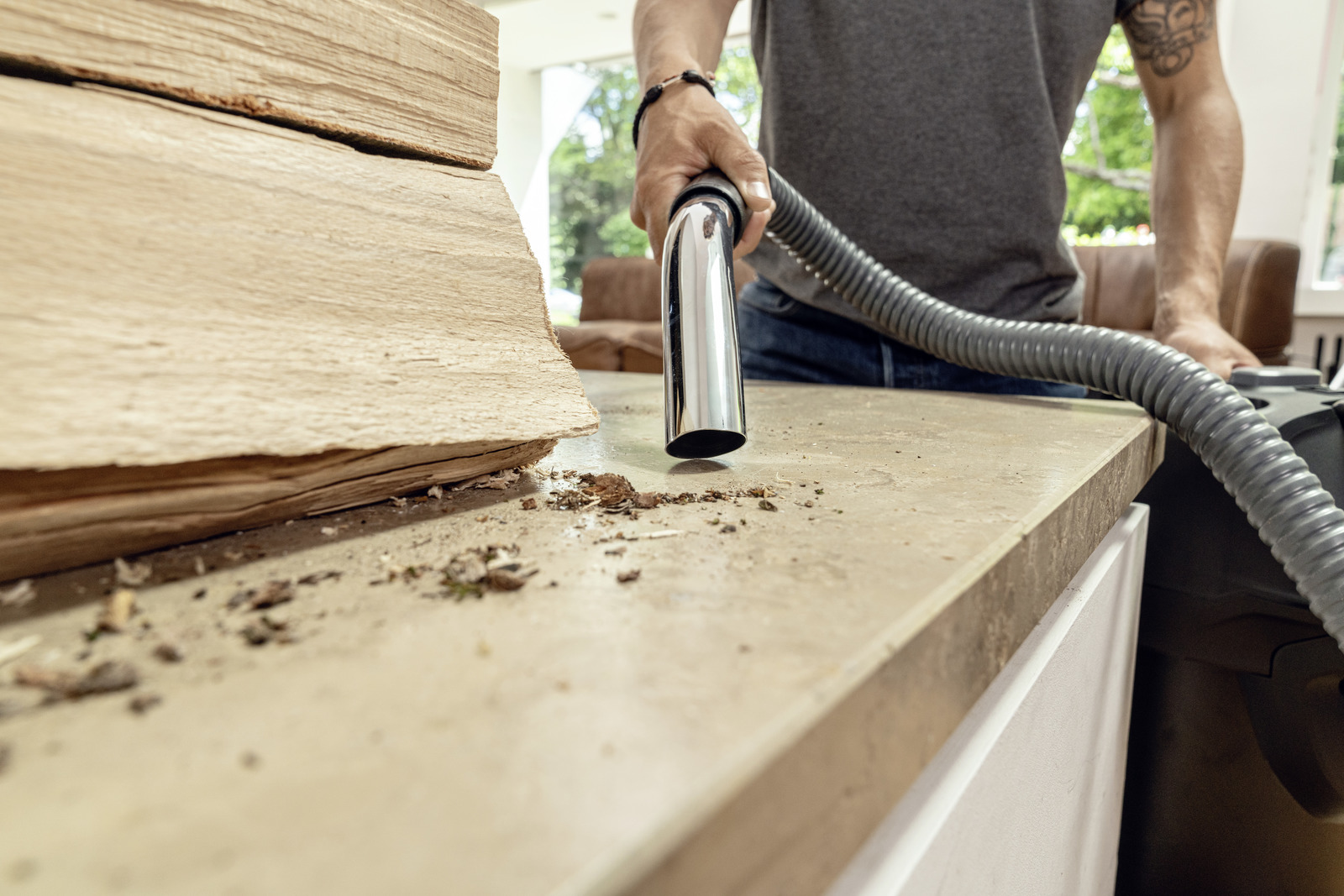 Persona che aspira un piano di lavoro con un aspirapolvere portatile. Legno e detriti.