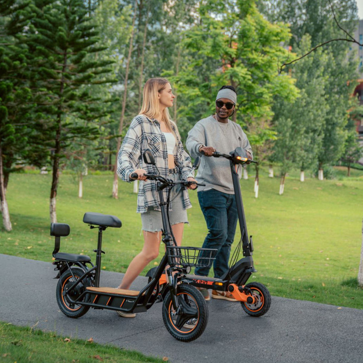 Para jeżdżąca na hulajnogach elektrycznych po ścieżce, z drzewami w tle, słoneczny dzień.