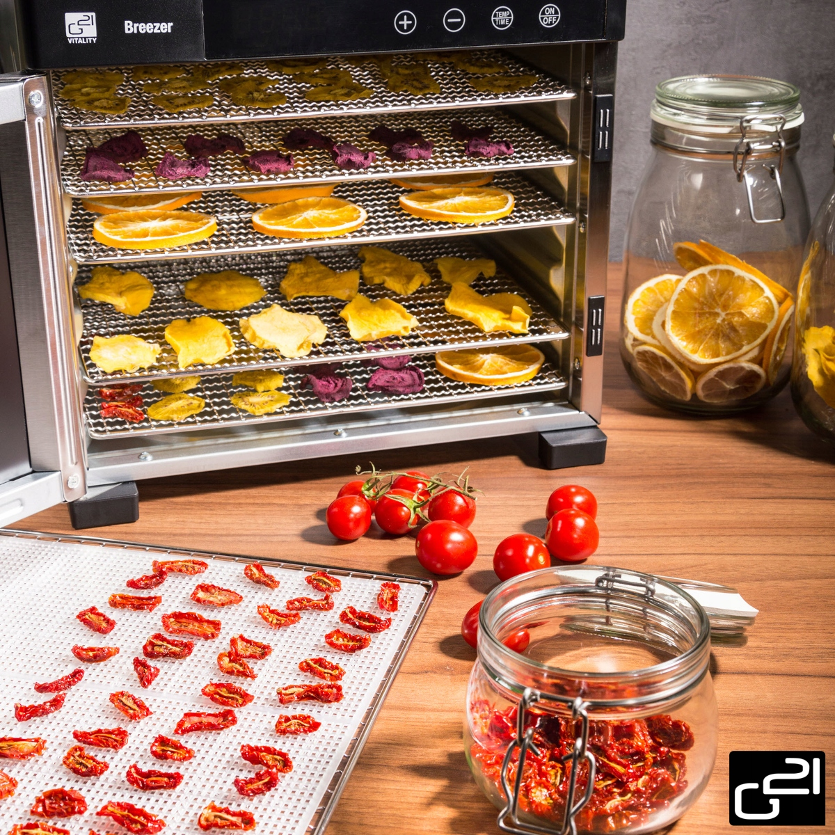 Suszarka do żywności z tacami suszonych pomidorów, plasterków pomarańczy i innych produktów, ze słoikami.