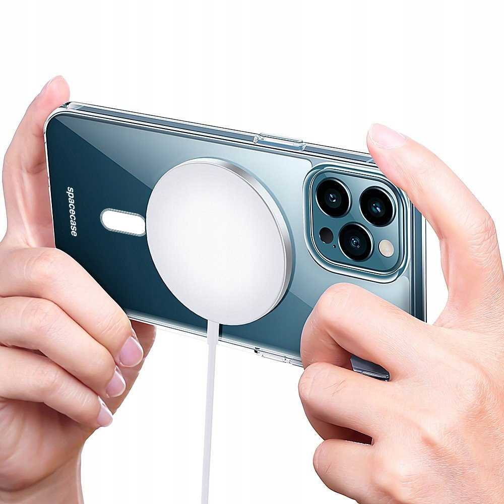 Dłonie trzymające telefon z przezroczystym etui i białym pierścieniem magnetycznym, z kablem ładującym.