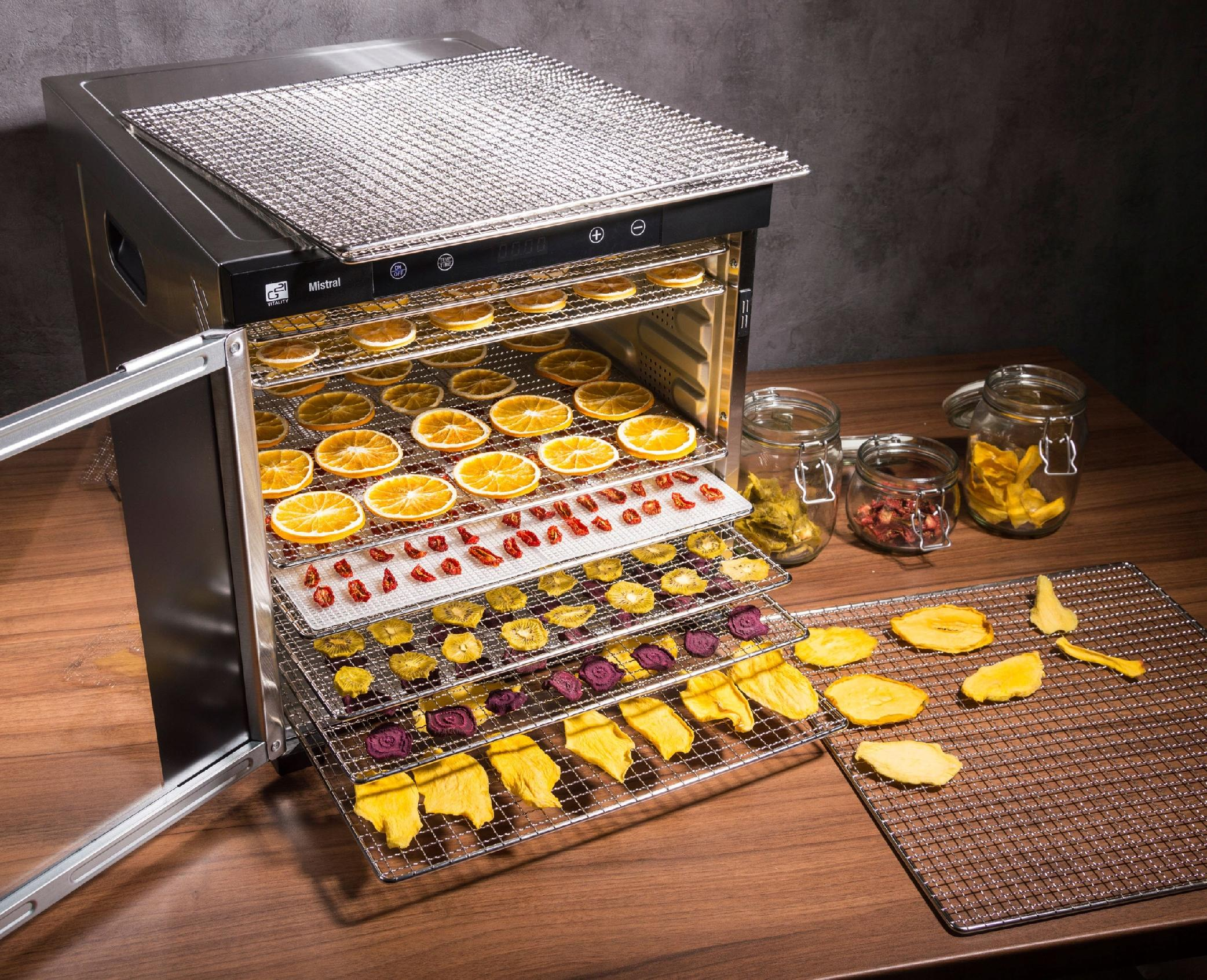 Suszarka do żywności z suszonymi owocami i warzywami na tacach.