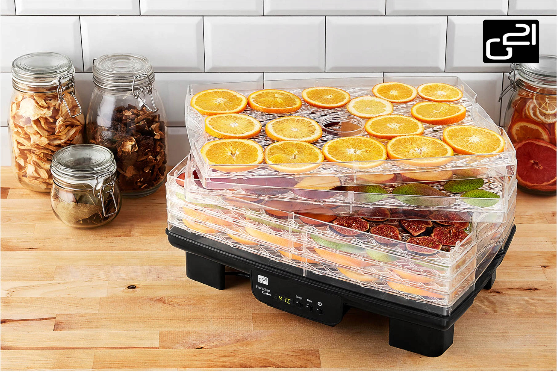 Dehydrator żywności wypełniony plastrami pomarańczy i figami. Słoiki z suszonymi owocami z boku.