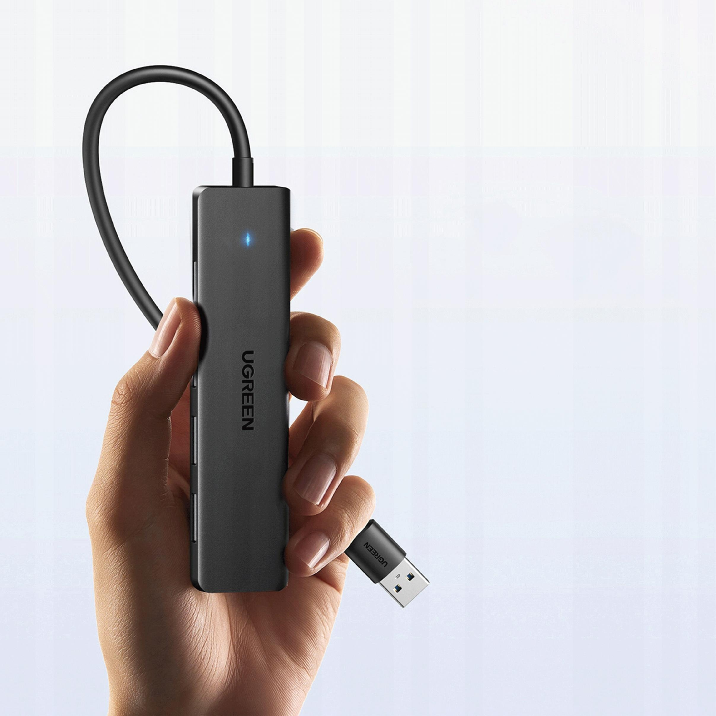 Una mano che tiene un hub USB nero con il logo 'UGREEN'. È visibile un connettore USB.